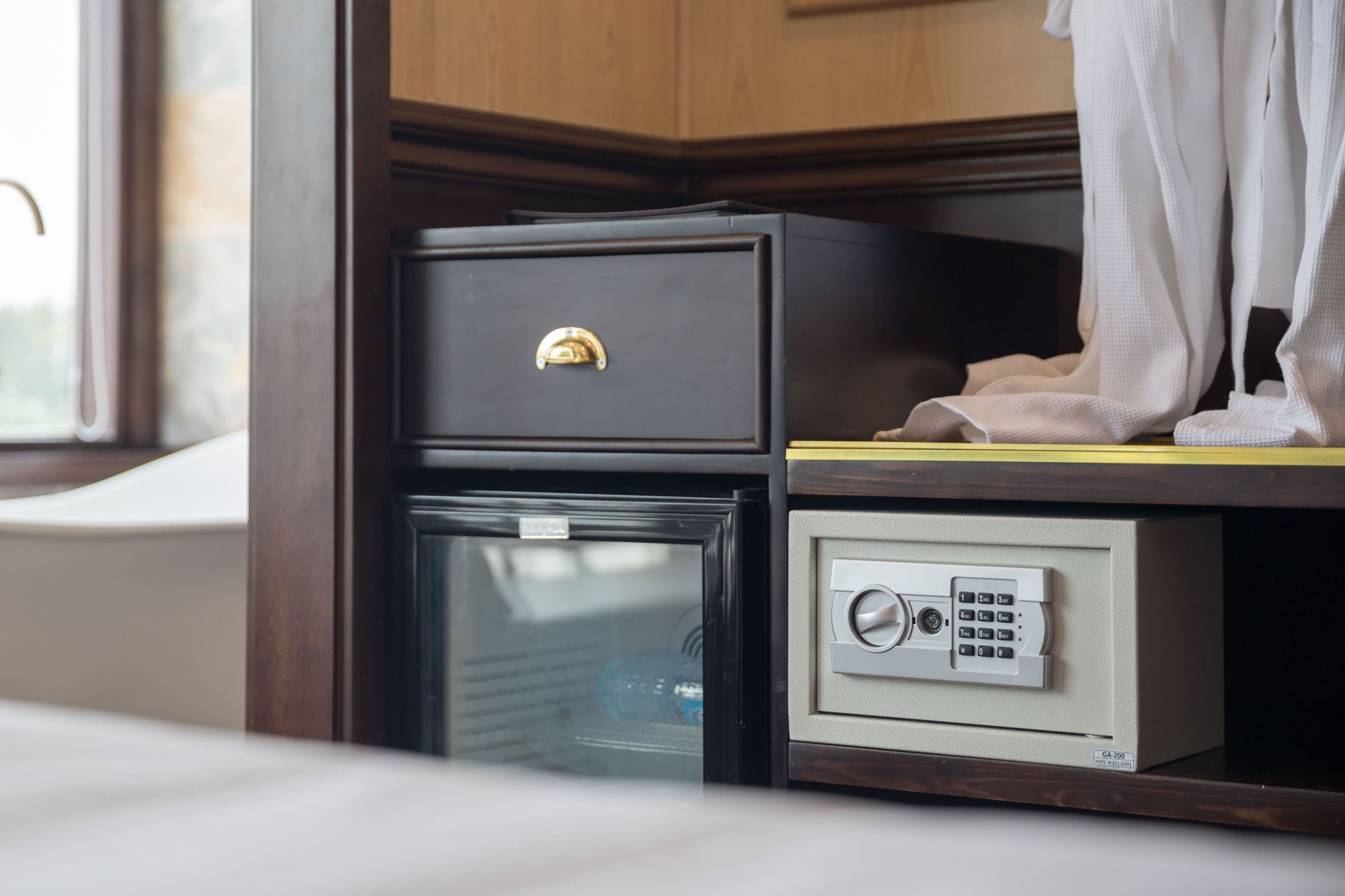 A small safe with a combination dial and a lockable drawer, located in a wooden cabinet with a window in the background.
