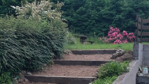 Een reeks buitenstappen van steen die leiden naar een tuin met grindpaden en verschillende planten.