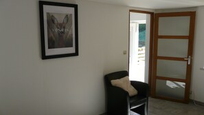 Una habitación con un cuadro en la pared, una silla con cojín y una puerta que da al exterior.