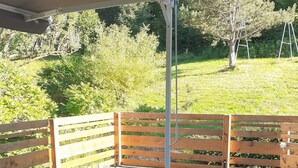 Een terras buiten met een houten eettafel, omringd door een houten schutting en een overdekt gedeelte.