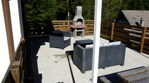 Een terras buiten met twee donkergrijze banken, een kleine tafel en een steenoven.
