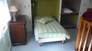 Een slaapkamer met een bed, een houten stoel, een bureau met een lamp en een klein plankje.