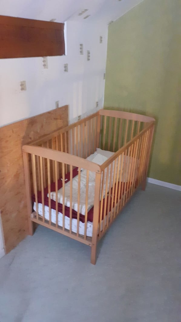 A wooden crib with a mattress and pillows, positioned against a wall with a green painted surface and a white ceiling.
