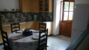 Een keuken met een eettafel voor vier personen, houten kastjes, een koelkast en een raam met uitzicht op groen.