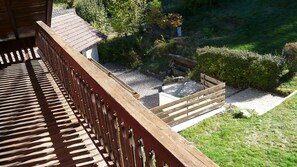 Eine Holzterrasse mit Geländer, ein kleiner Gartenbereich mit einer Bank und ein Gebäude mit einem Ziegeldach.