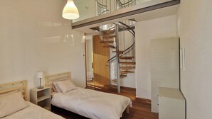 Ein Schlafzimmer mit zwei Betten, einem Nachttisch, einer Lampe und einer Wendeltreppe.