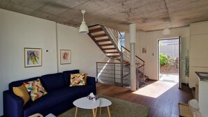Ein Wohnzimmer mit blauem Sofa, weißem Couchtisch, einer Treppe und Blick ins Freie.