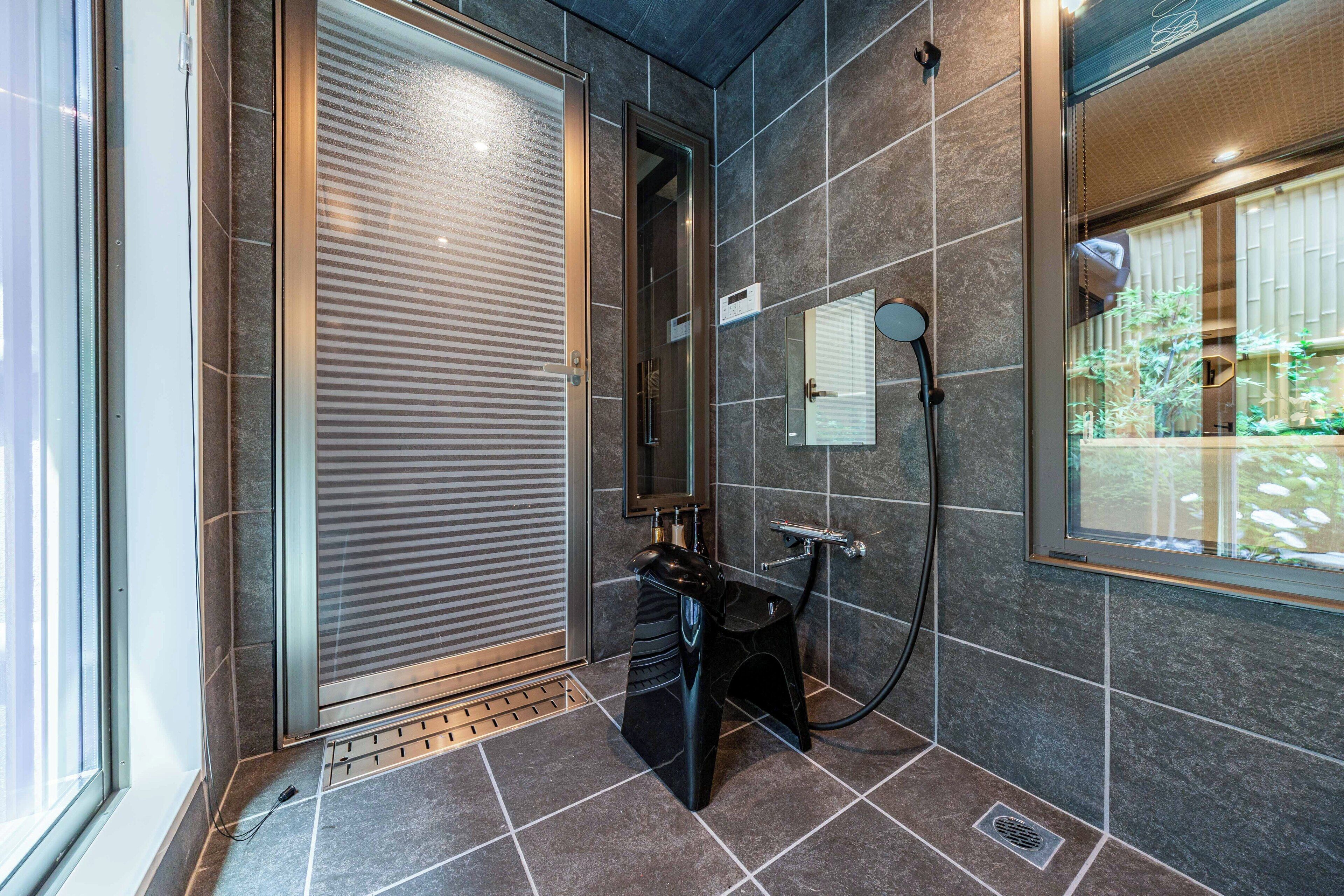 A modern bathroom with a glass door, a shower area, and a window with a view of greenery.