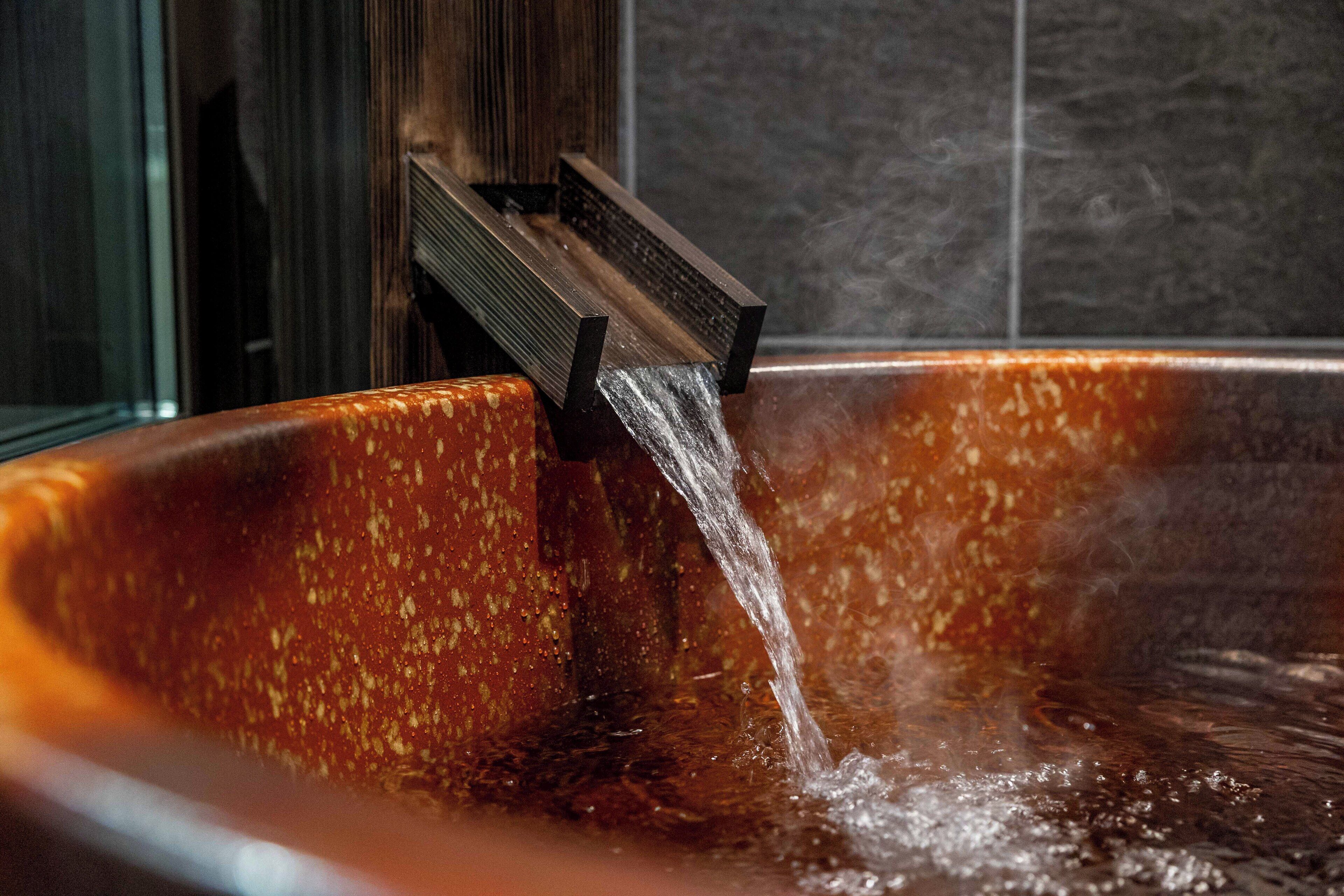 A hot tub with water flowing from a wooden structure.