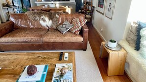 A modern living room with a brown leather sofa, a wooden coffee table with magazines, a remote control, and a small plant. - Cosy “Mod” in Clunes  (Clunes)