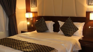 A neatly made bed with a patterned bedspread, two bedside lamps, and a headboard with a framed picture. - Pestana Hotel & Suites 3 (Riyadh)