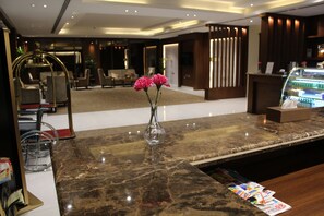 A hotel reception area with a marble counter, a vase with flowers, and a display of magazines. - Pestana Hotel & Suites 3 (Riyadh)