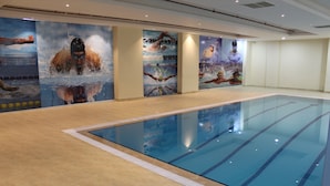 An indoor swimming pool with clear lanes, a tiled floor, and large murals depicting swimmers. - Pestana Hotel & Suites 3 (Riyadh)