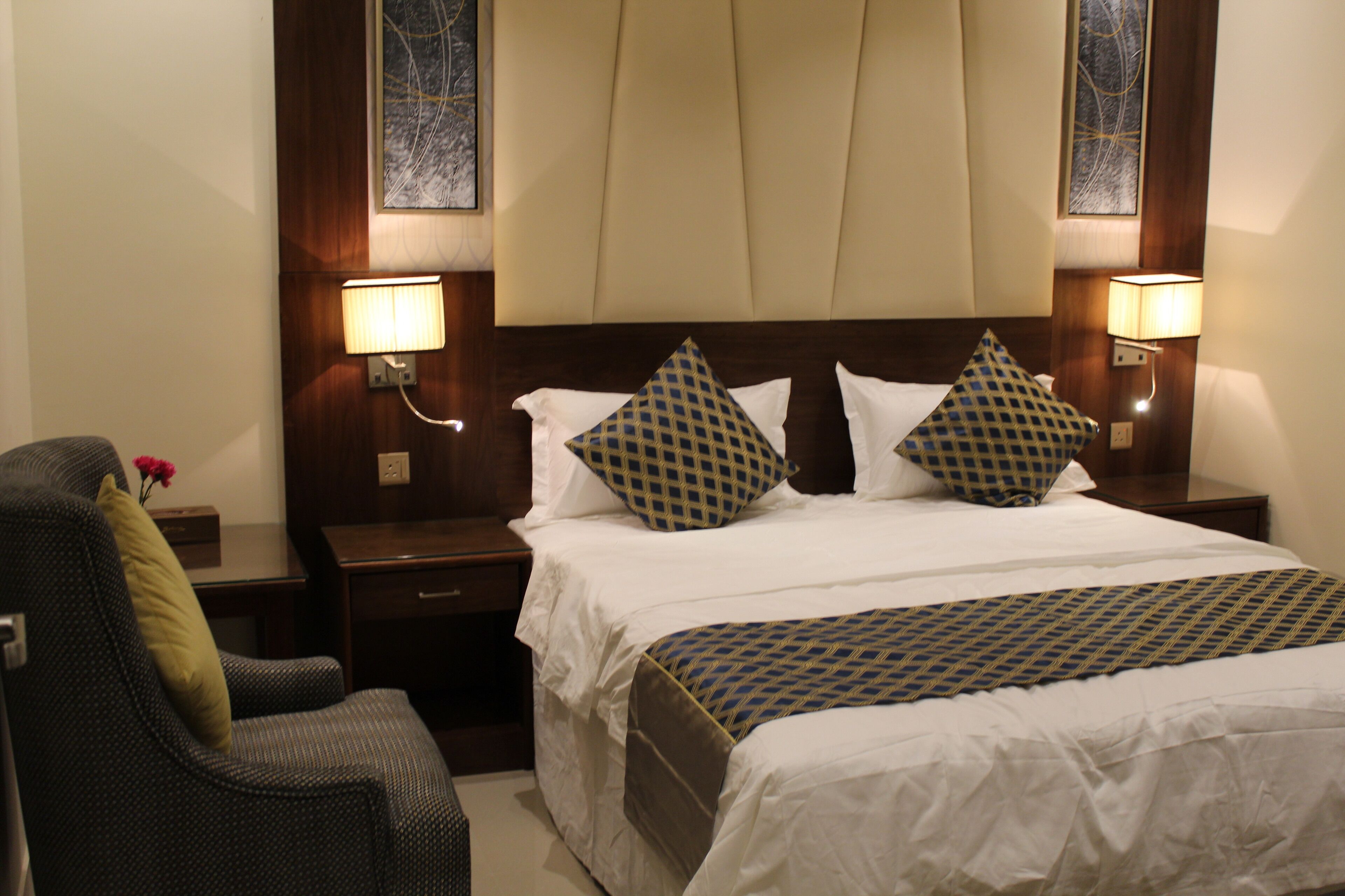 A hotel room with a large bed, two nightstands, a chair, and two wall-mounted lamps.