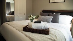 A neatly made bed with a white blanket, a decorative pillow, and a small basket with a towel.