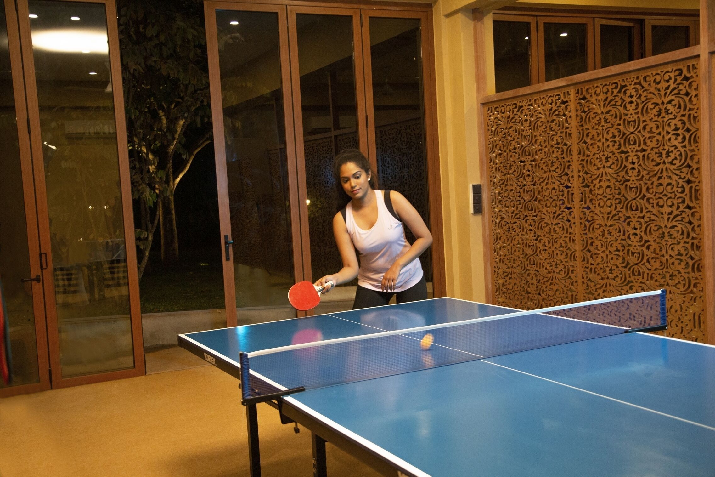 Un tavolo da ping pong con un giocatore che indossa una canotta bianca.