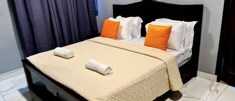 A neatly made bed with a beige quilt, two white pillows, and two orange pillows.