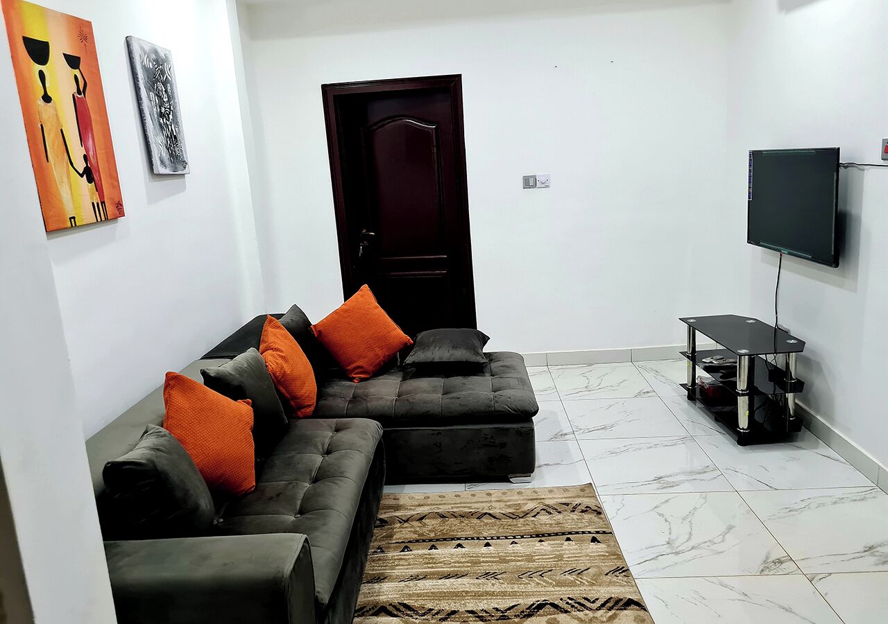 A living room with a sectional sofa, a flat-screen TV, a small table, and a door.