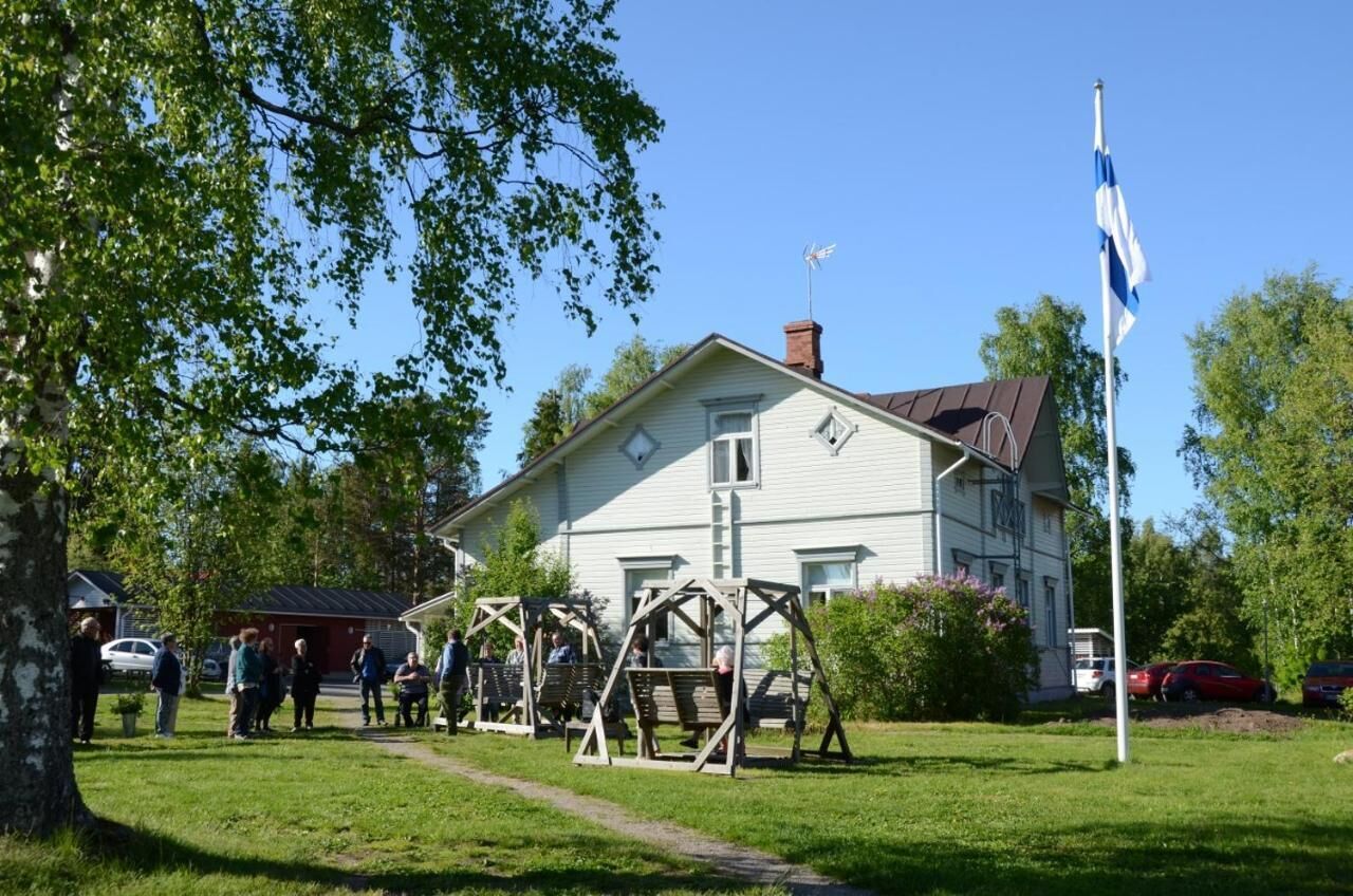 A white house with a chimney, a swing set, and a flagpole.
