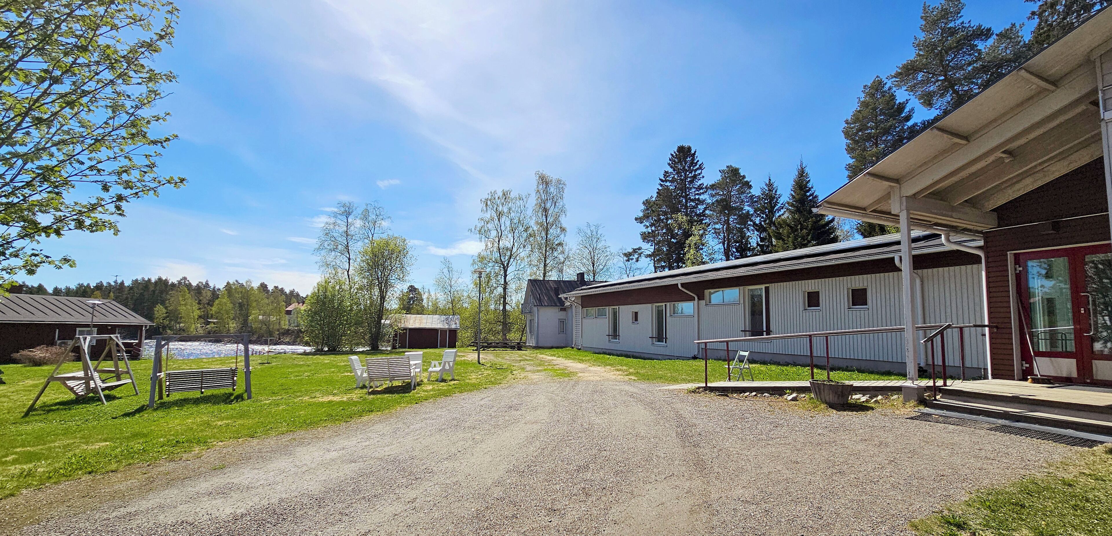 A gravel driveway leading to a building with a porch and outdoor seating area.