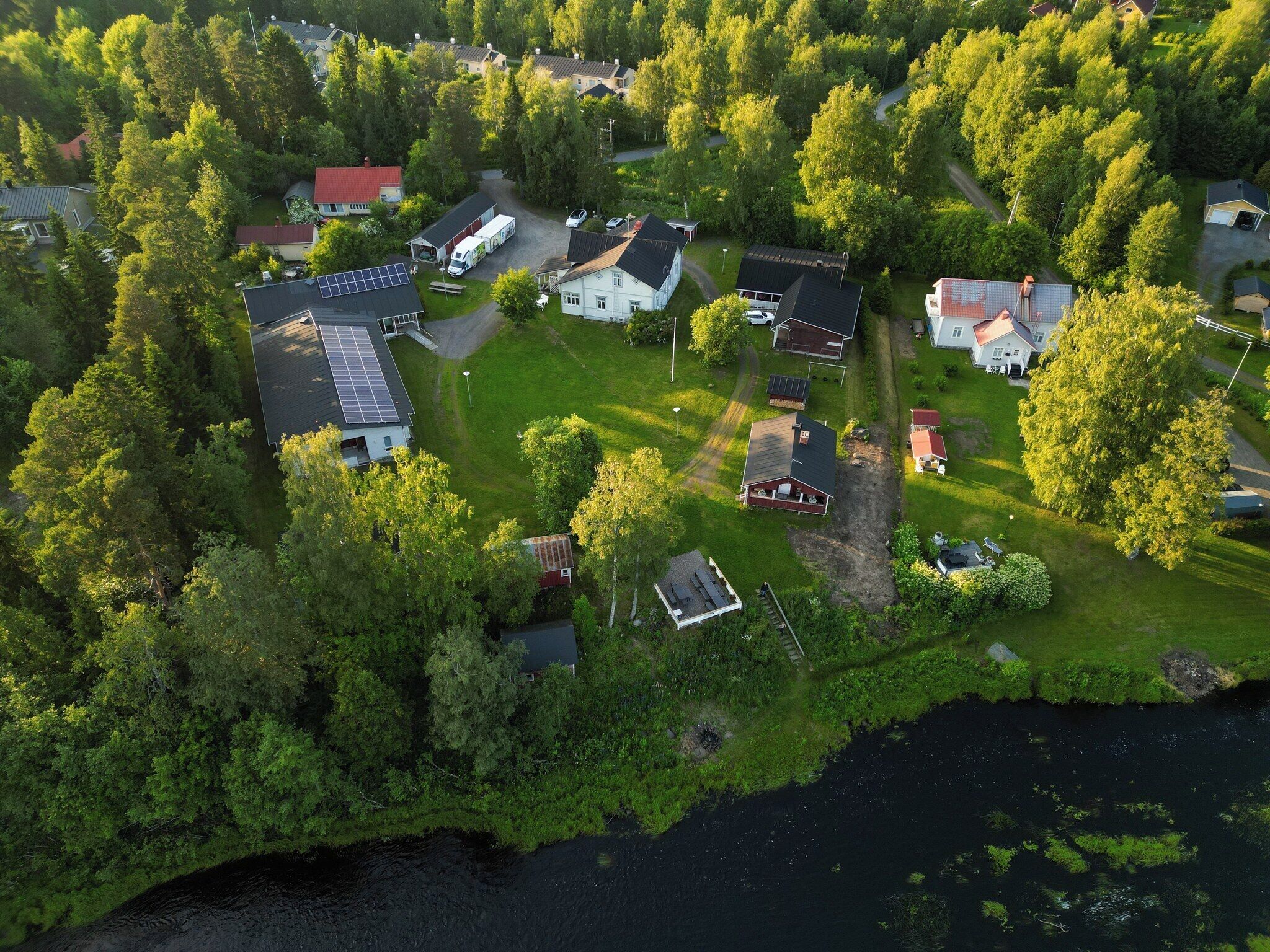 An aerial view of a residential area with houses, a solar panel installation, and a body of water.