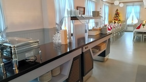 A buffet setup with a glass display case, stacked plates, and a Christmas tree in the background. - Taiga Resort (Oulu)