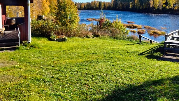 A lakeside cabin with a deck and a small building, surrounded by autumn foliage and a clear view of the lake. - Taiga Resort (Oulu)