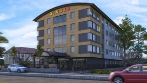 Um hotel de vários andares chamado GINGER, com design arquitetônico moderno, apresentando uma entrada imponente e uma área de estacionamento na frente.