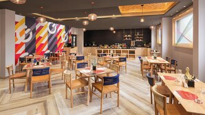 Um restaurante moderno com mesas e cadeiras de madeira, um revestimento de azulejos pretos e luminárias pendentes.