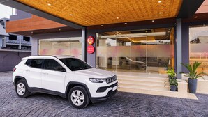 Um SUV branco estacionado em frente a um edifício com design moderno, com teto trabalhado e entrada de vidro.