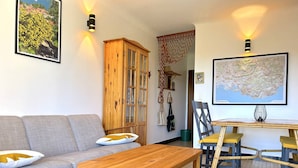 Ein Wohnzimmer mit einer Couch, einem Holztisch und Stühlen. Es gibt einen Schrank, eine Karte an der Wand und eine Lampe.
