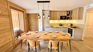 Une cuisine moderne avec des meubles en bois, une table à manger pour six personnes et des luminaires suspendus.