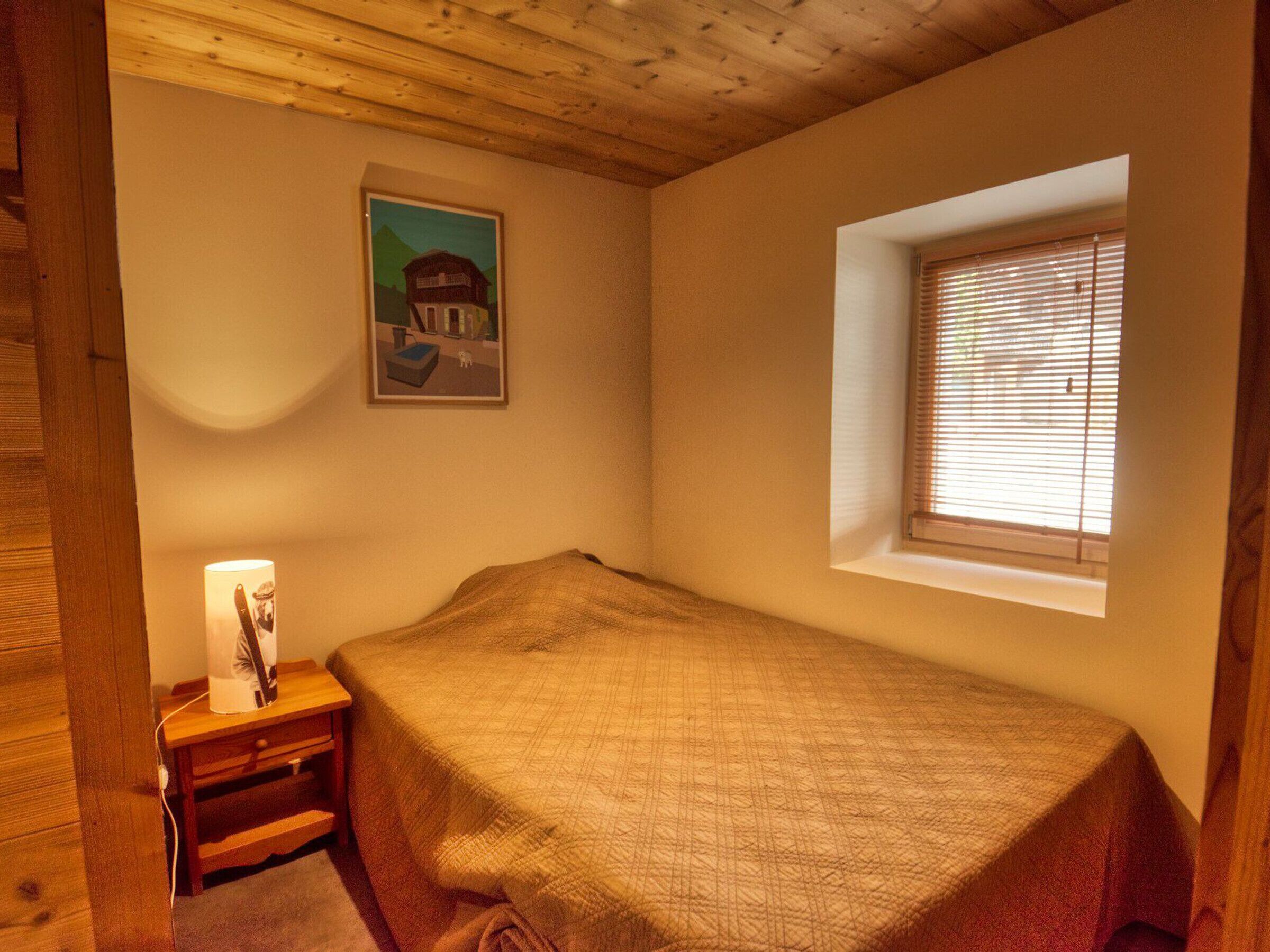 Quarto com uma cama de solteiro, mesa de cabeceira, luminária, janela com persianas e um quadro na parede.