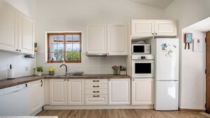 A modern kitchen with white cabinets, a wooden countertop, a built-in dishwasher, a microwave, an oven, and a refrigerator. - Traditional Algarve home with private pool, air con & solar, near Praia Marinha (Lagoa)