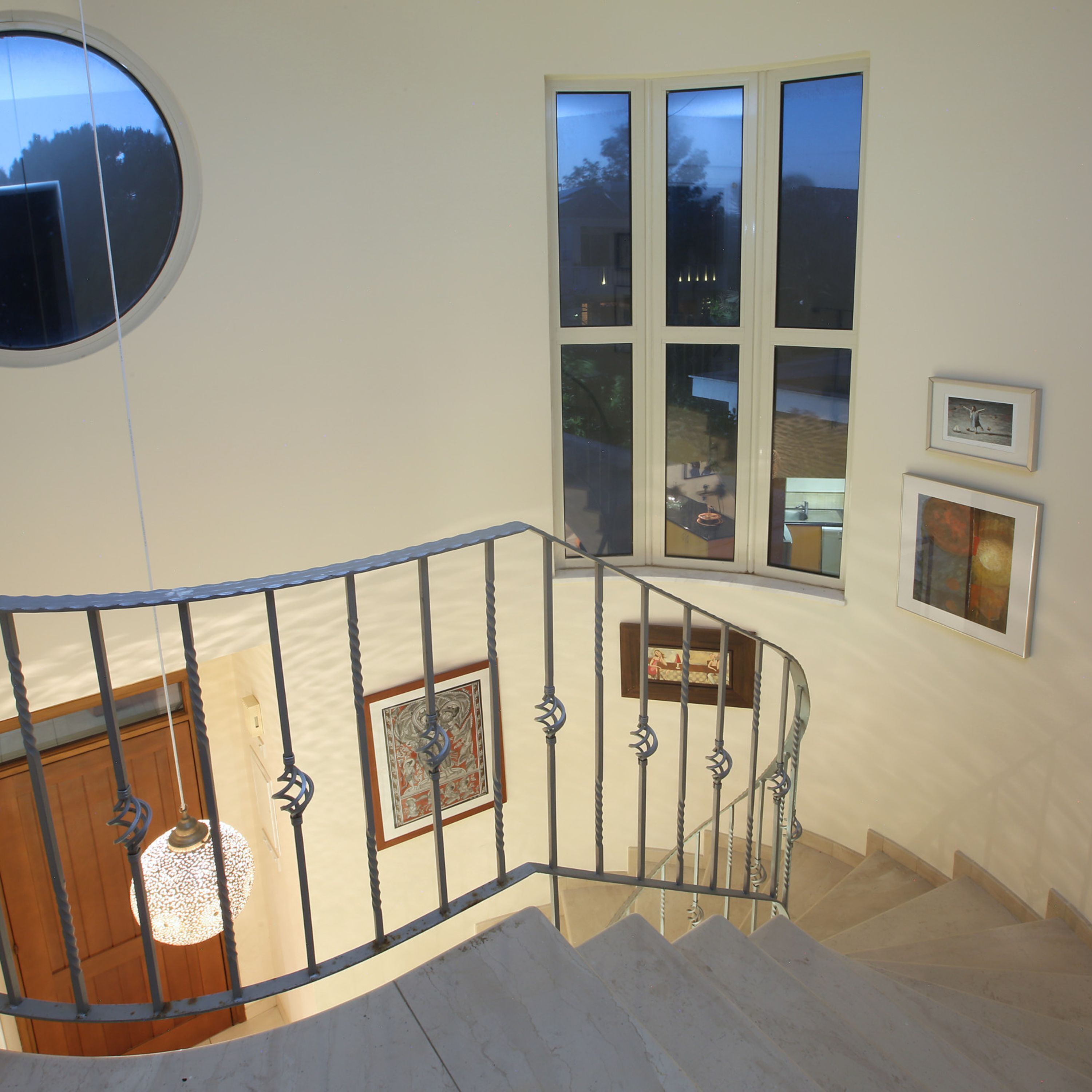 A staircase with a metal railing, a round mirror, and a view of the outside through large windows.
