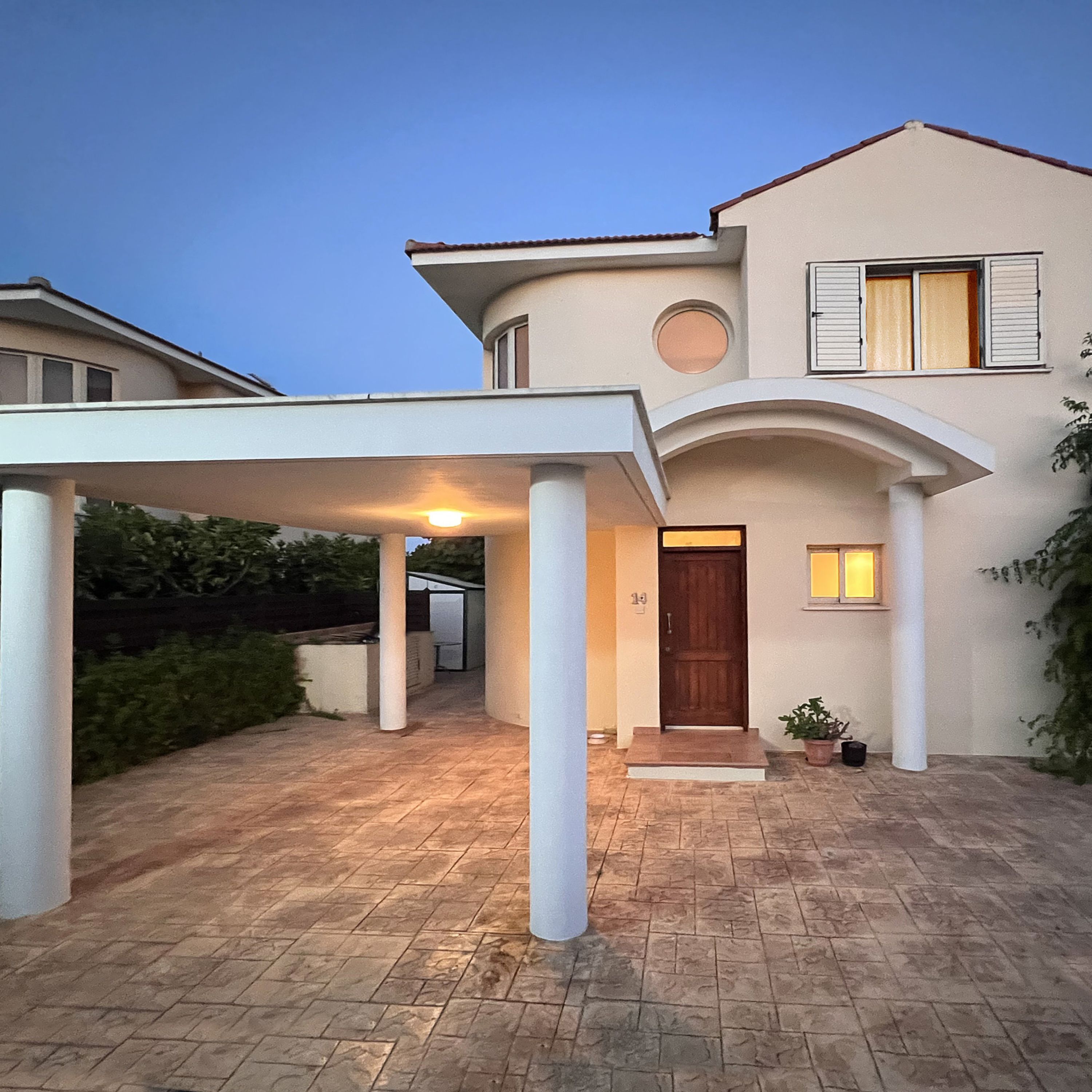A two-story house with a covered driveway, a wooden front door, and a small garden area.