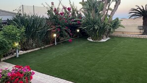 A well-maintained garden with artificial grass, various plants, and a pathway. - Larnaca Chelidonia Seafront Villa (Pervolia)