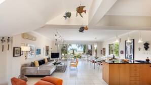 A spacious living area with a sofa, orange armchair, and a dining area with a kitchen island. - Larnaca Chelidonia Seafront Villa (Pervolia)