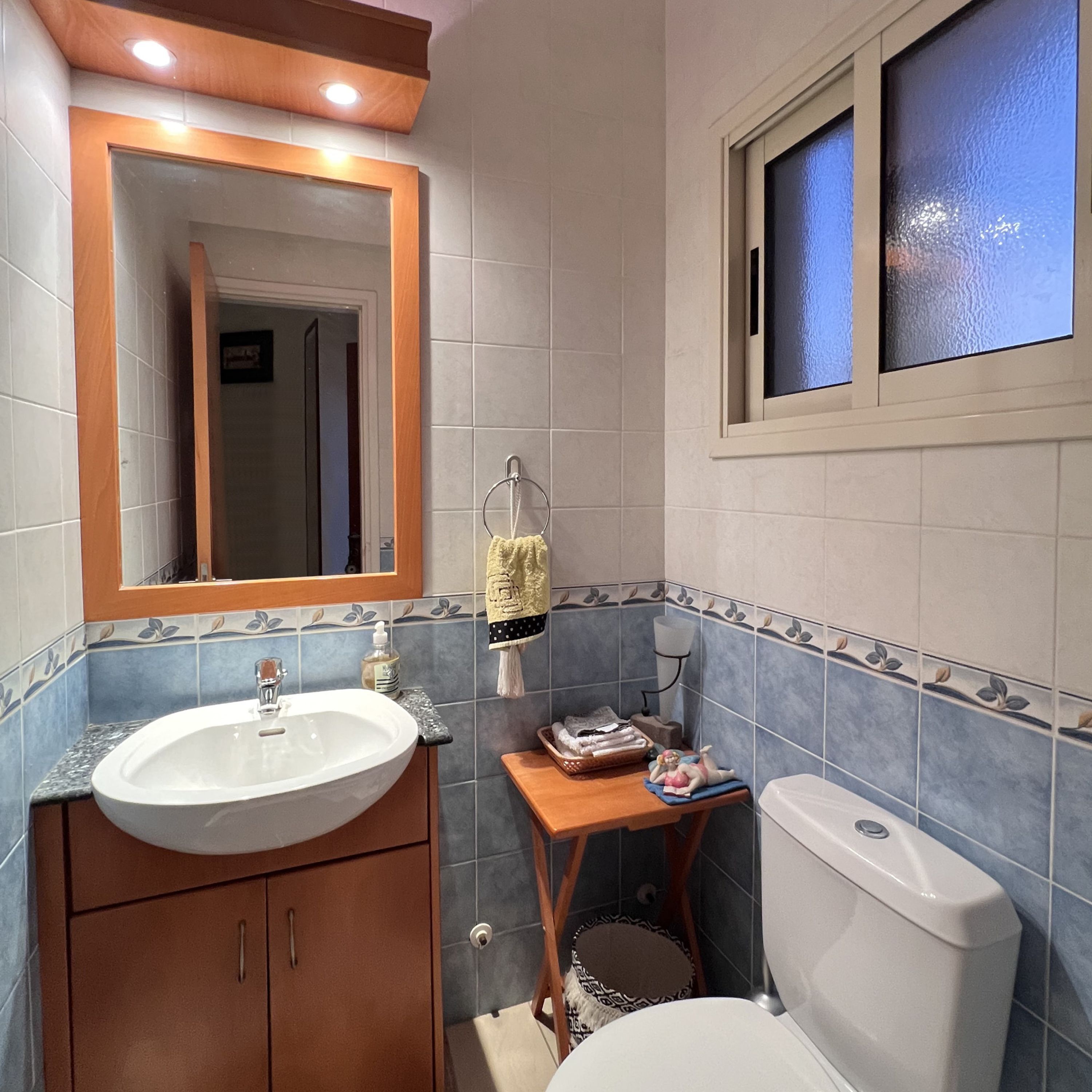 A bathroom with a sink, mirror, toilet, and a window.