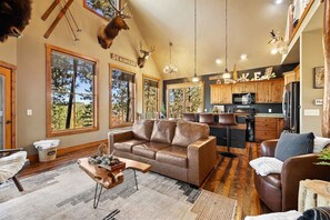 A spacious living room with a leather sofa, a wooden coffee table, and a large window offering a view of trees.