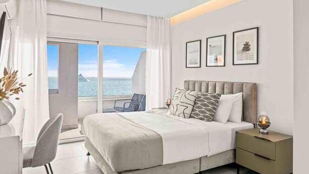 Una habitación de hotel moderna con una cama grande, un escritorio y una silla. Hay tres cuadros en la pared y una ventana con vista al mar.