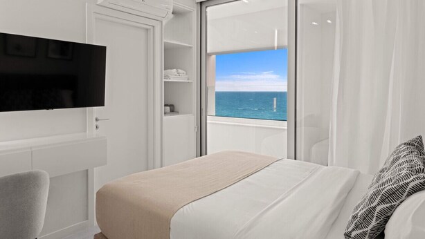 Een moderne hotelkamer met een bed, een televisie, een kledingkast en een balkon met uitzicht op zee.