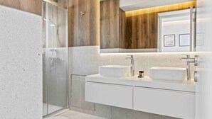 A modern bathroom with a glass shower enclosure, two sinks, and a large mirror. - Coastal Seaside Residences 04 (Limassol)