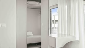 Una habitación con armario empotrado, ventana con cortinas traslúcidas y vistas a edificios.