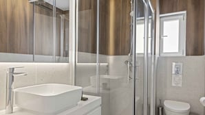 Ein modernes Badezimmer mit einem großen weißen Waschbecken, einer gläsernen Dusche und einer Toilette.