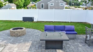 Une terrasse extérieure avec un foyer en pierre, une table à plateau en verre et un ensemble de meubles de jardin comprenant un canapé bleu.