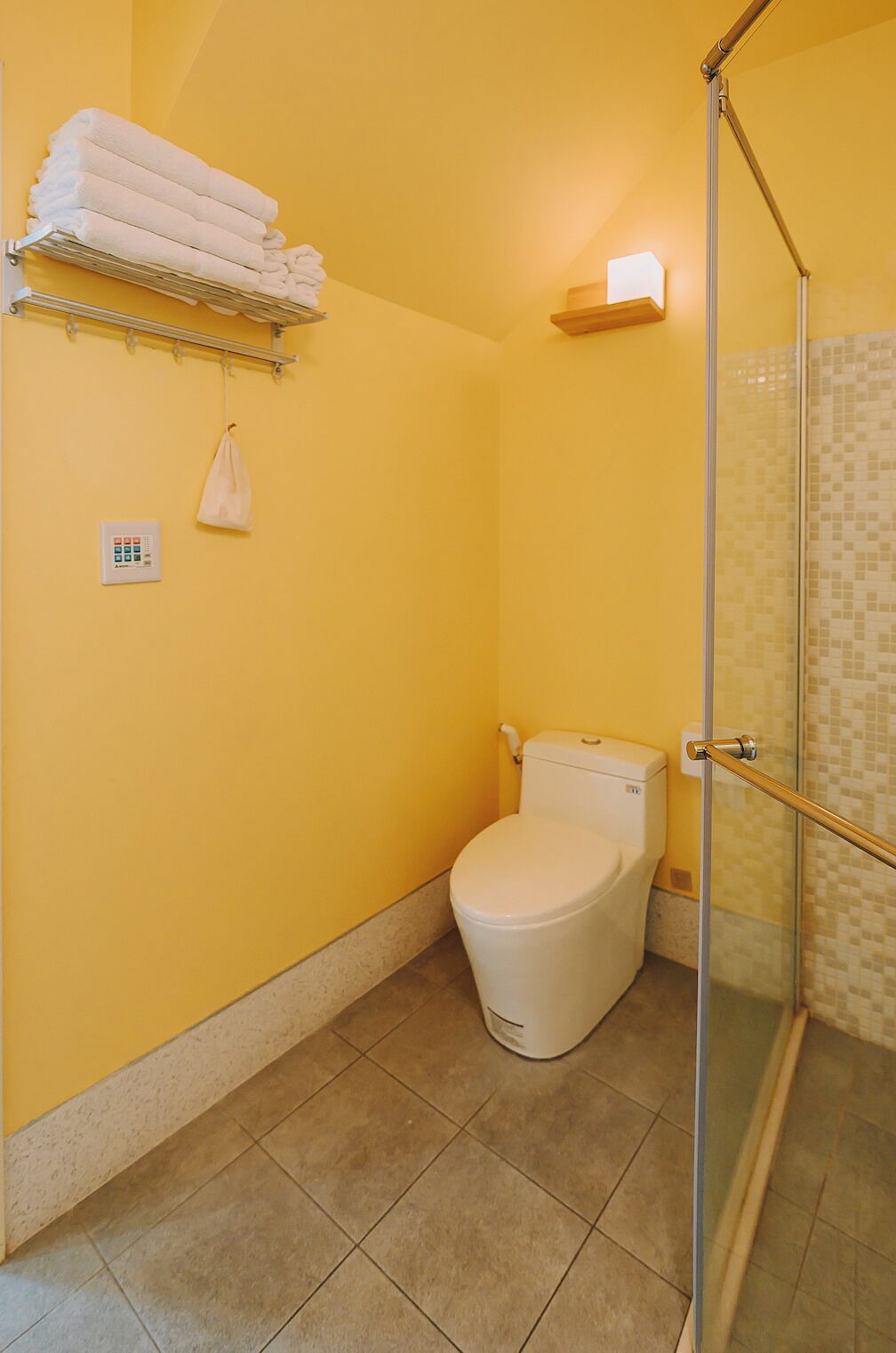 A bathroom with a toilet, a glass shower enclosure, and a towel rack with folded towels.