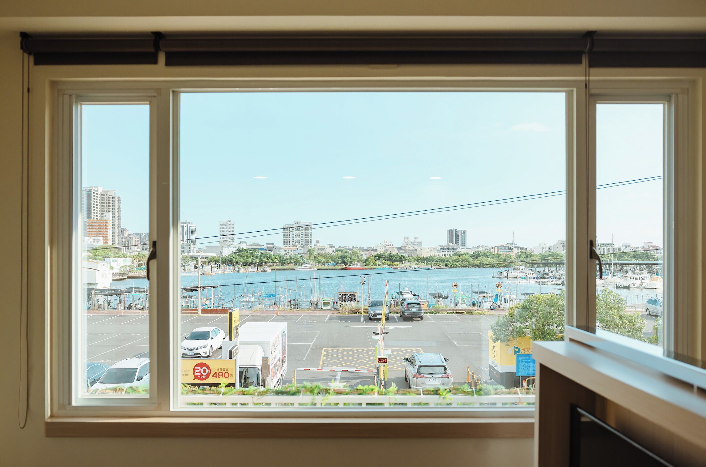 A view from a window overlooking a parking lot with a marina and city buildings in the background.