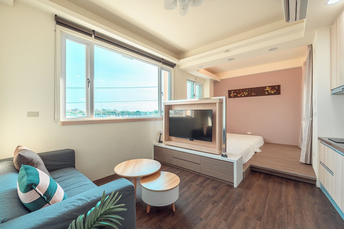 A modern living room with a sofa, a TV, a small table, and a bed.