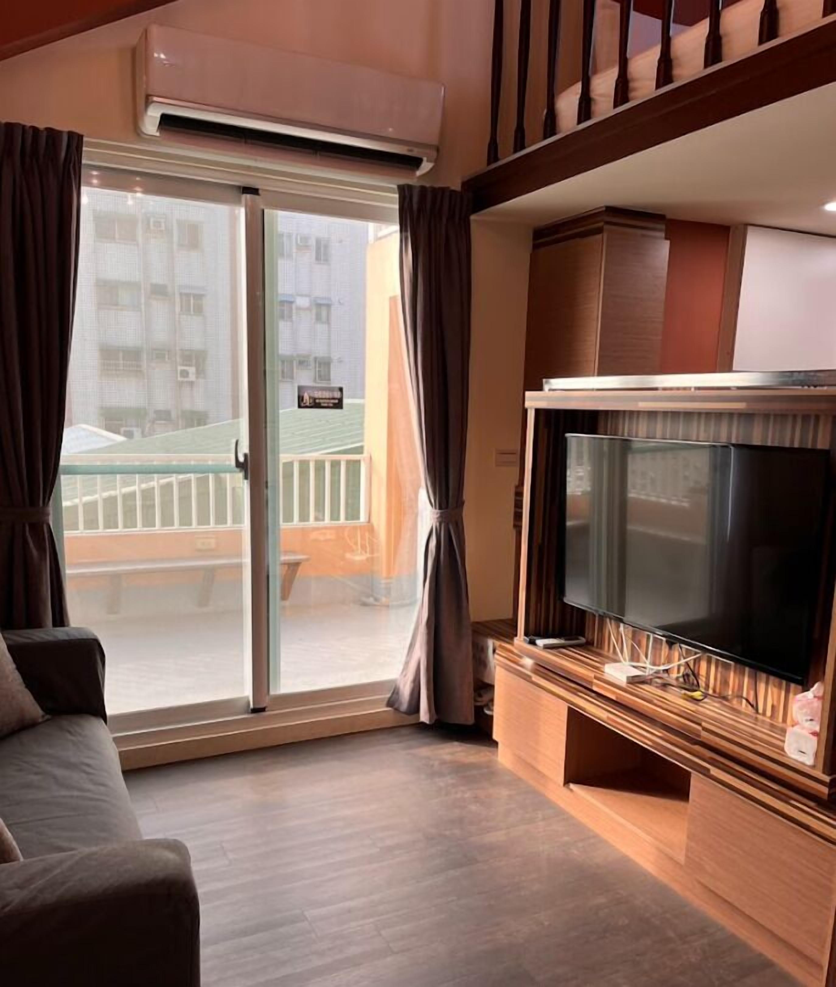 En stue med et stort fladskærms-tv, en sofa og en skydedør, der fører til en balkon.
